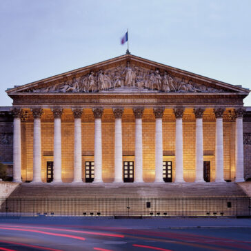 The Assemblée Nationale in Paris illuminated at dusk, a popular destination for travelers booking New York to Paris business class flights.